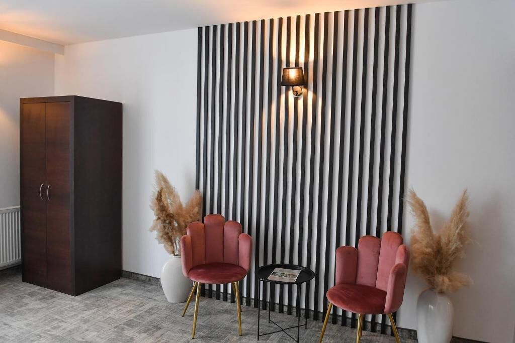 A modern room with a dark wooden wardrobe, two red chairs, a small round table, and a wall with vertical black and white stripes.