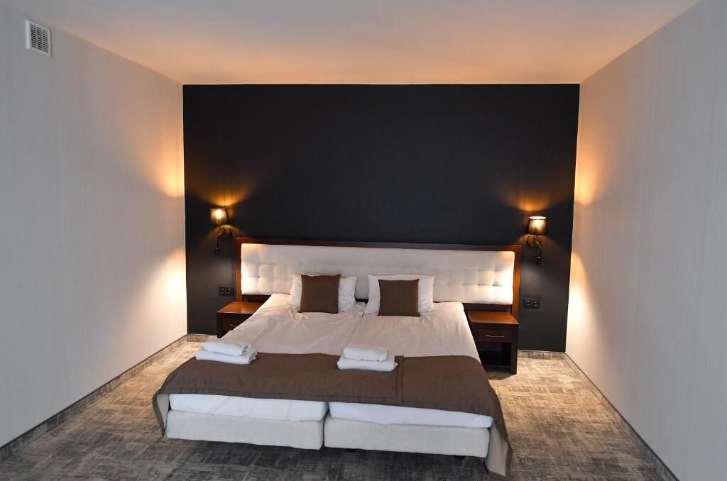 A hotel room with a large bed, two bedside tables, and wall-mounted lamps.