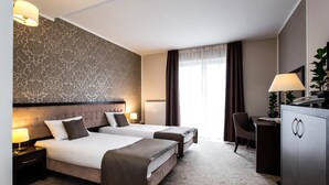 Habitación de hotel con dos camas, un escritorio, una silla y un amplio ventanal con cortinas.