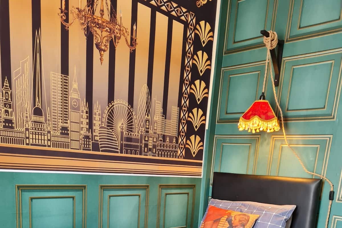 A bedroom with a cityscape mural, a black headboard, a patterned bedspread, and a nightstand with drawers.