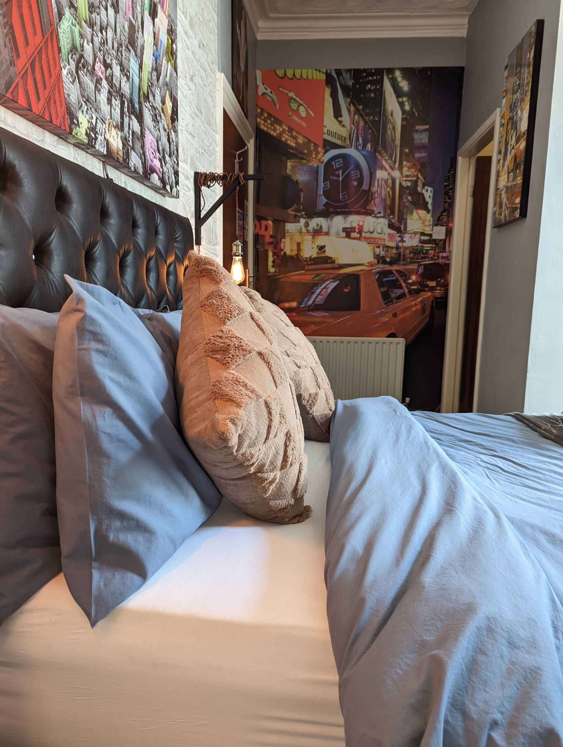 A bed with a tufted headboard, two pillows, and a wall mural of a cityscape.