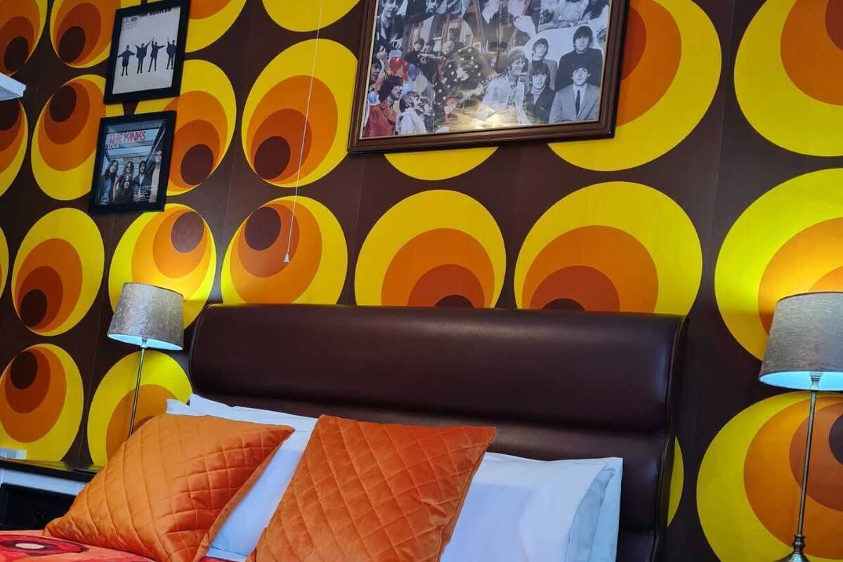 A hotel room with a circular patterned wall, a bed with orange bedding, and two bedside lamps.
