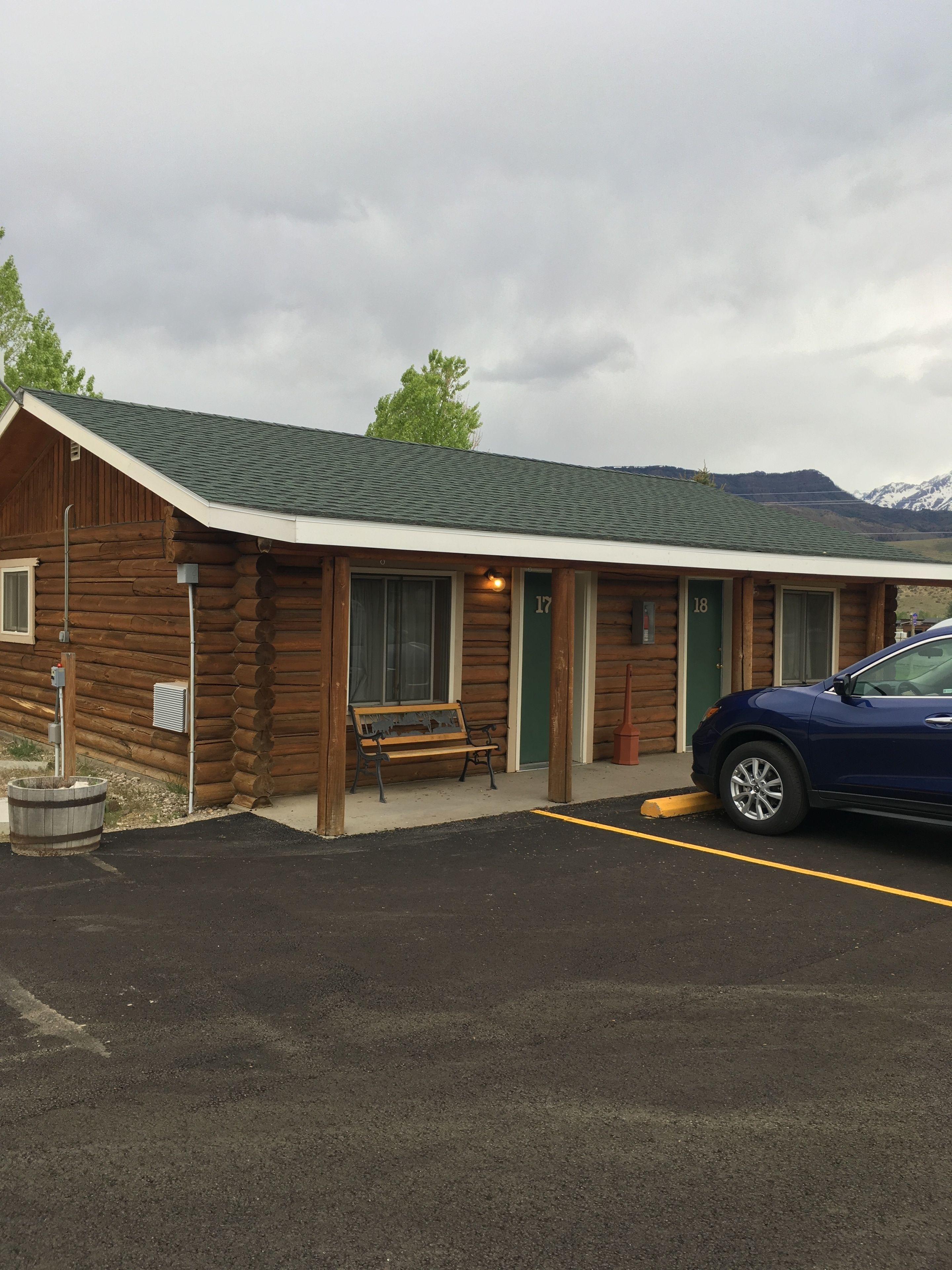 A log cabin with two numbered rooms, a bench outside, and a car parked in front.