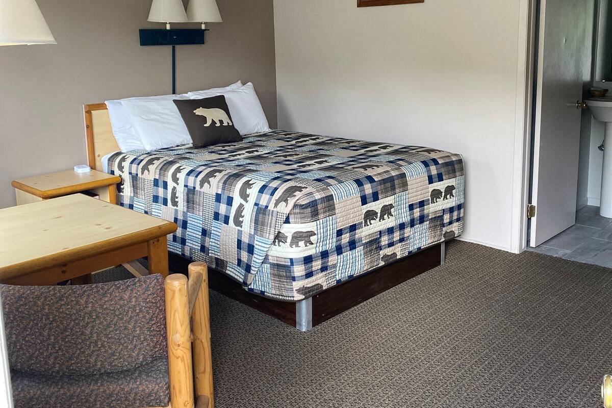 Habitación de hotel con cama, escritorio, silla, lámpara y un cuadro en la pared.