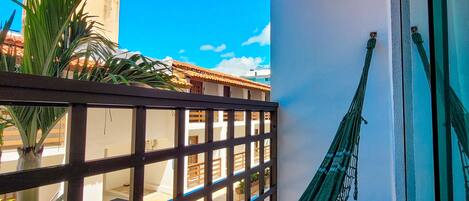 A balcony with a hammock, a view of a building, and a clear blue sky.