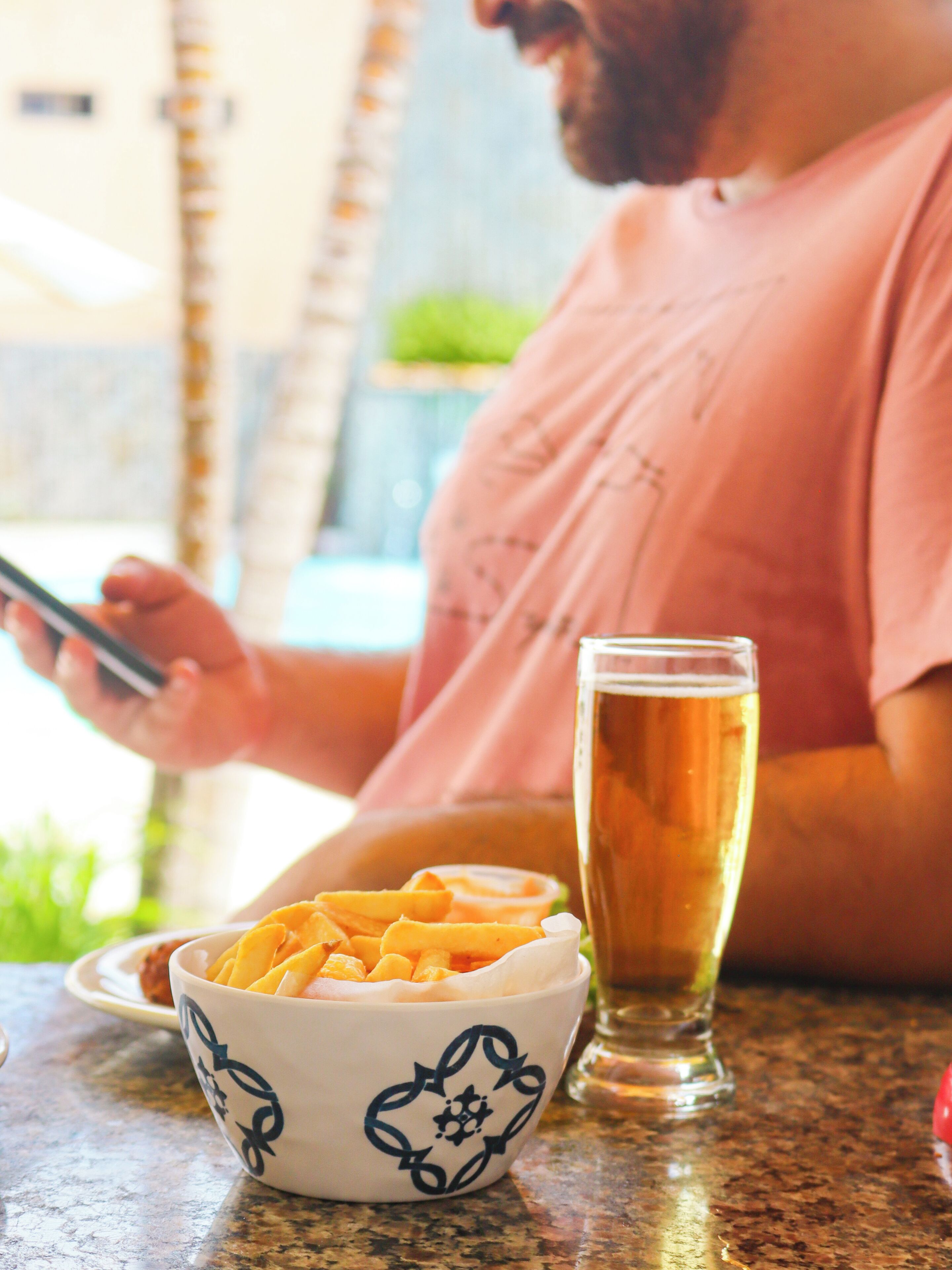 Iemand zit aan een tafel met een schaal eten en een glas bier.
