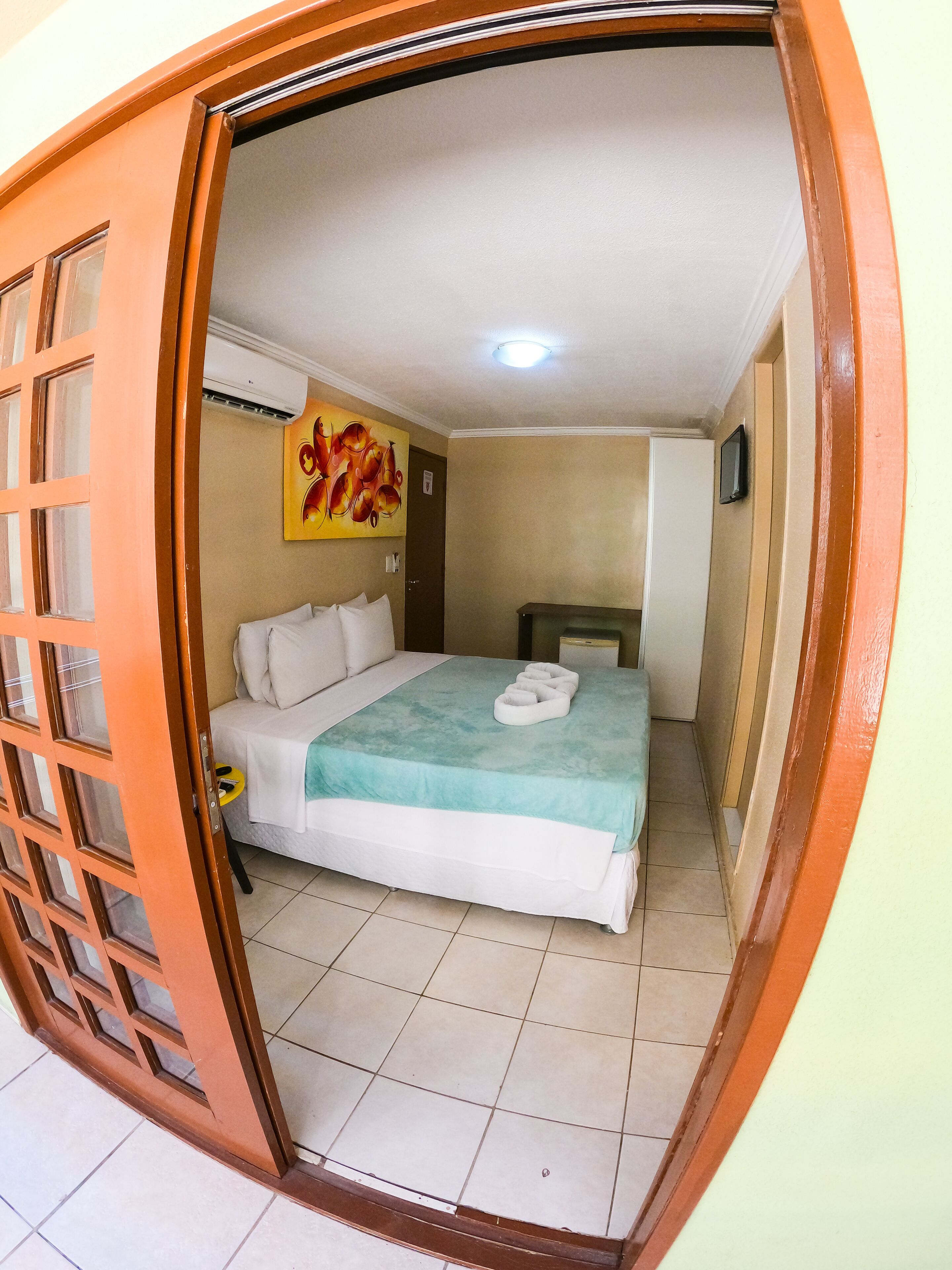 A hotel room with a bed, a painting on the wall, and a television on the wall.