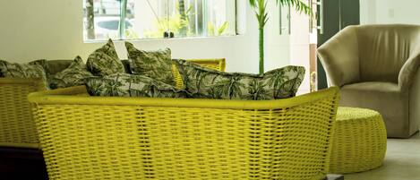 A modern living room with a yellow wicker sofa, a potted plant, and a beige armchair.