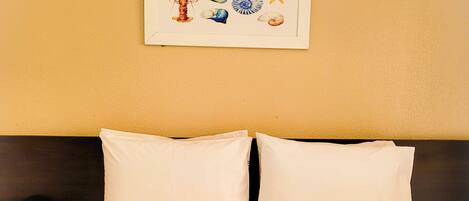 A hotel room with a bed, two pillows, a framed picture on the wall, and a towel rack with towels.