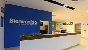 A reception desk with a blue wall and a sign that reads "Bienvenido te estamos esperando." - One Silao (Silao)