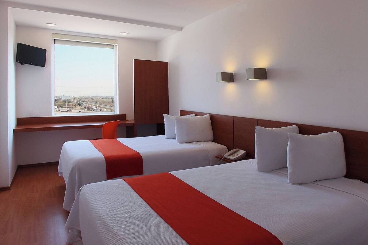 Habitación de hotel con dos camas, un escritorio, una silla, un televisor y una ventana con vistas.