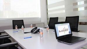A conference room with a white table, two black chairs, a laptop displaying a graph, and several water bottles. - One Silao (Silao)