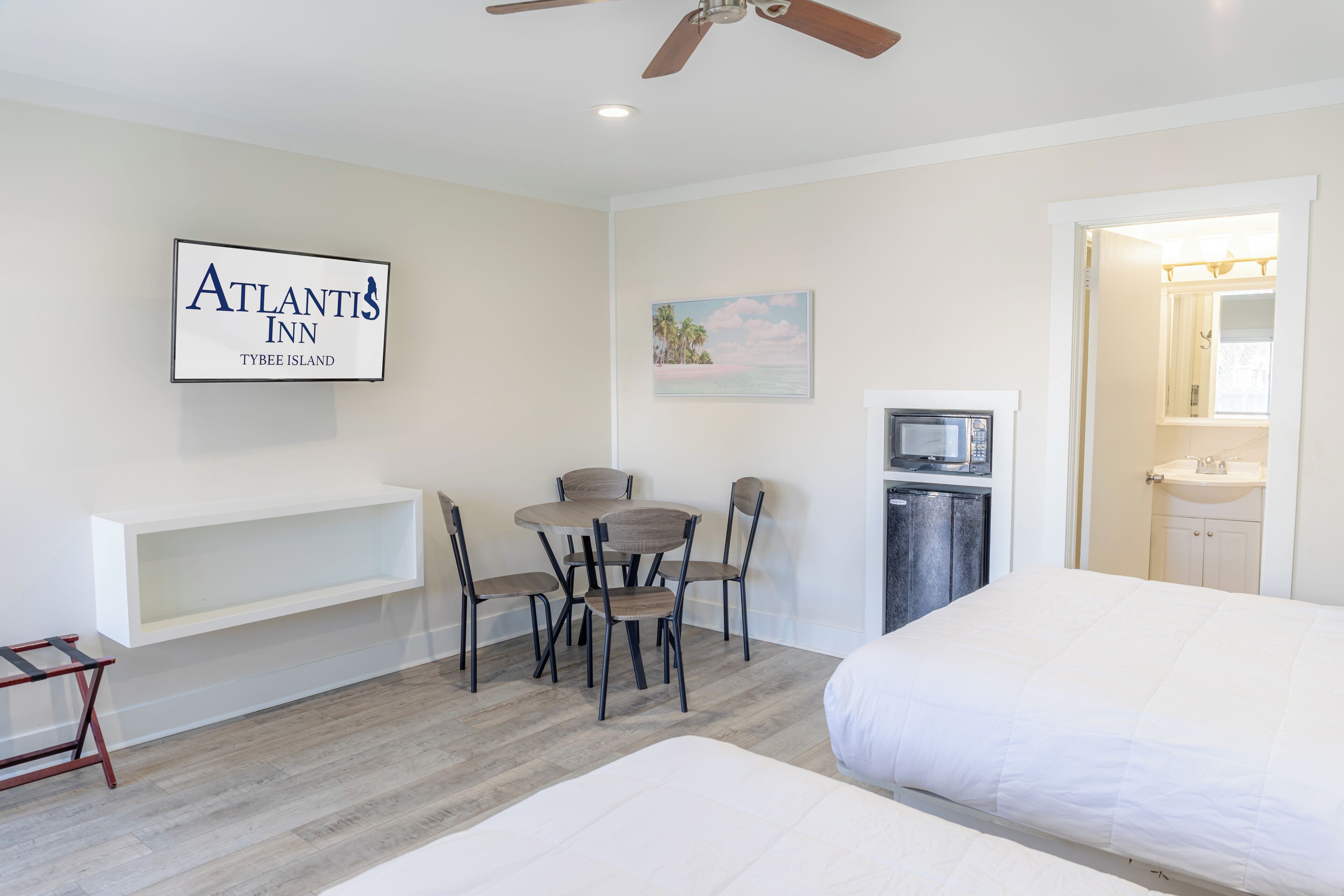 A hotel room with a bed, a desk with chairs, a microwave, and a sink.