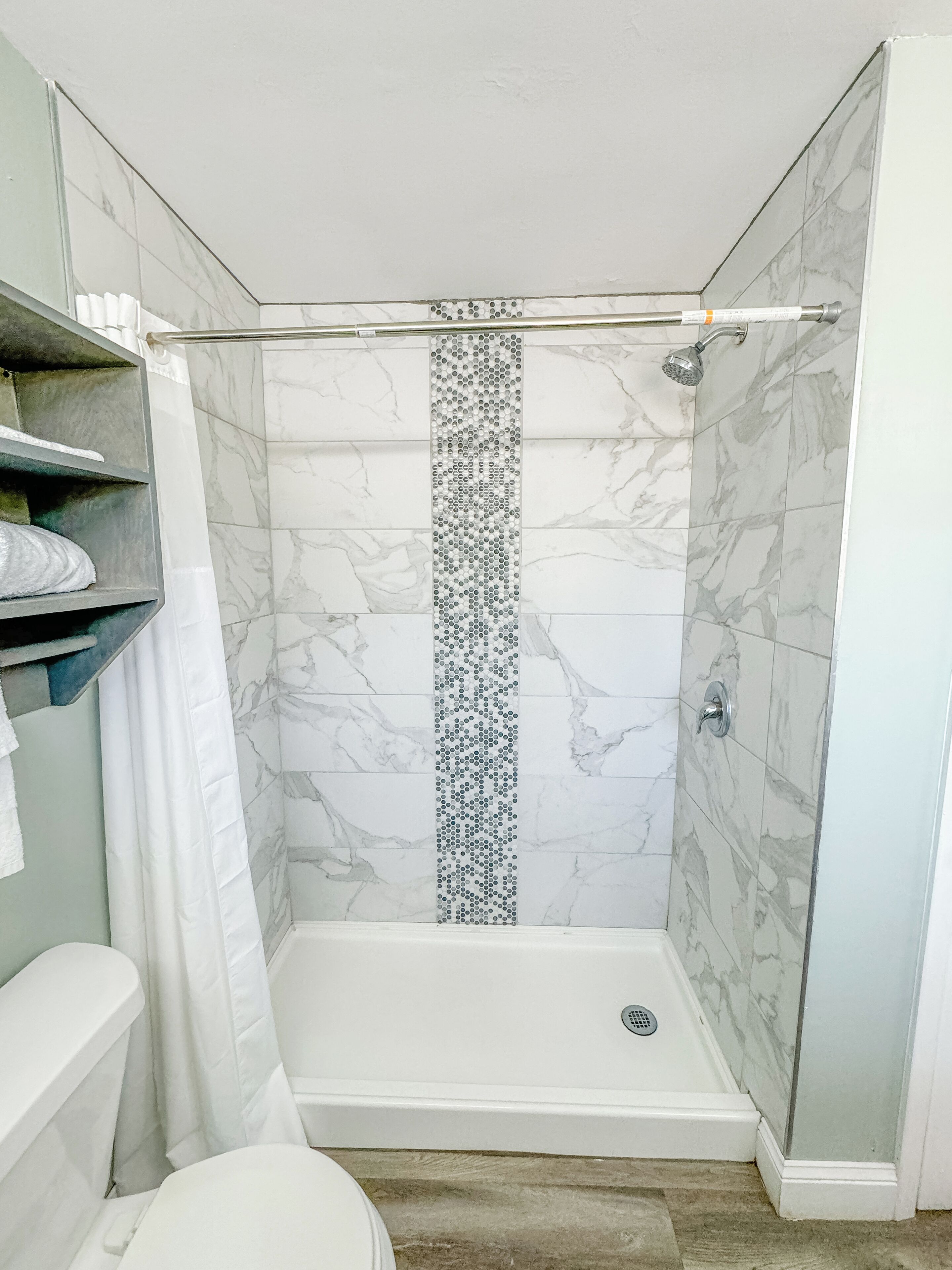 A shower with a glass door, a white bathtub, and a marble-tiled shower wall.