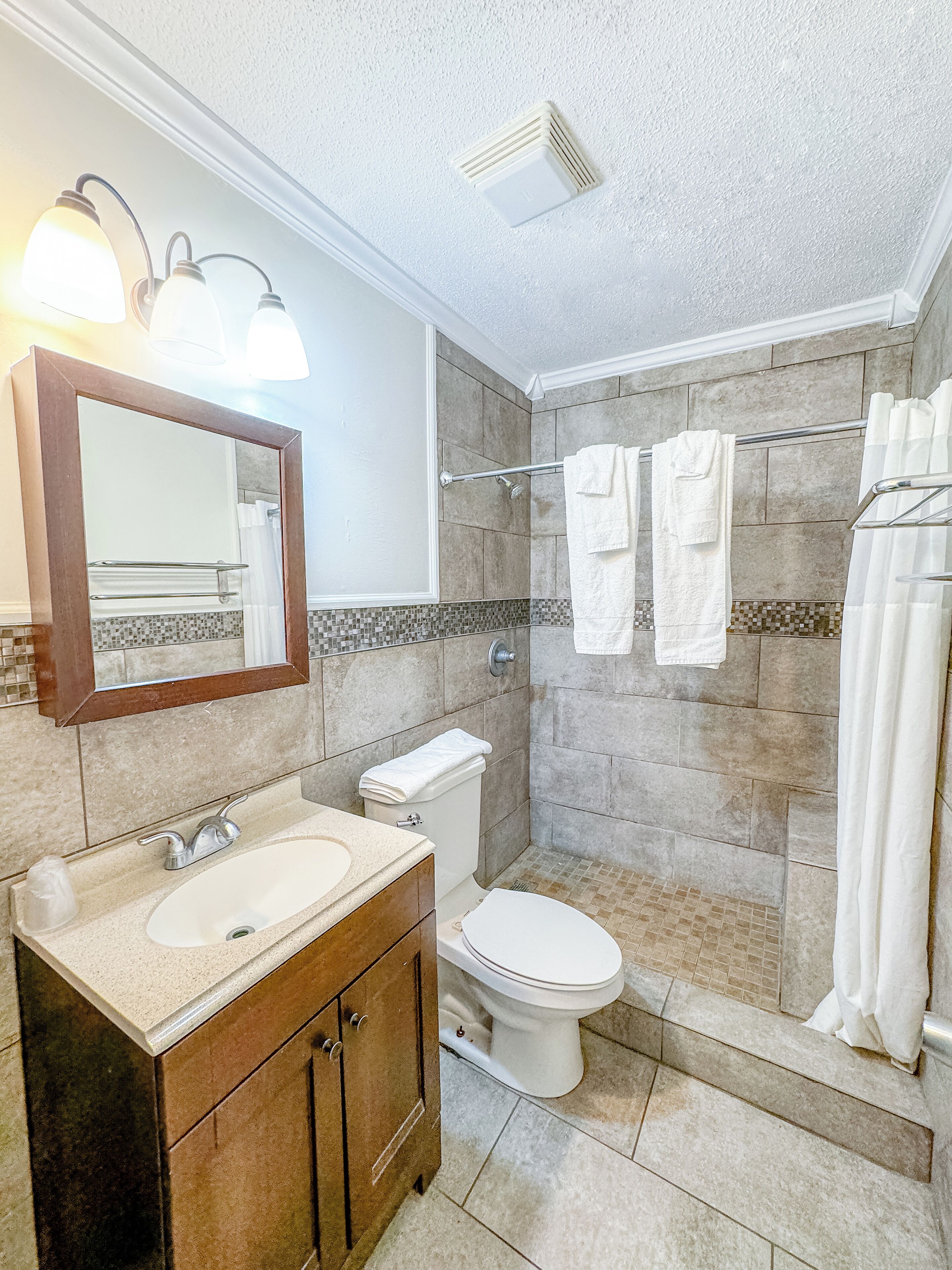 A bathroom with a sink, mirror, toilet, shower, and towel rack.