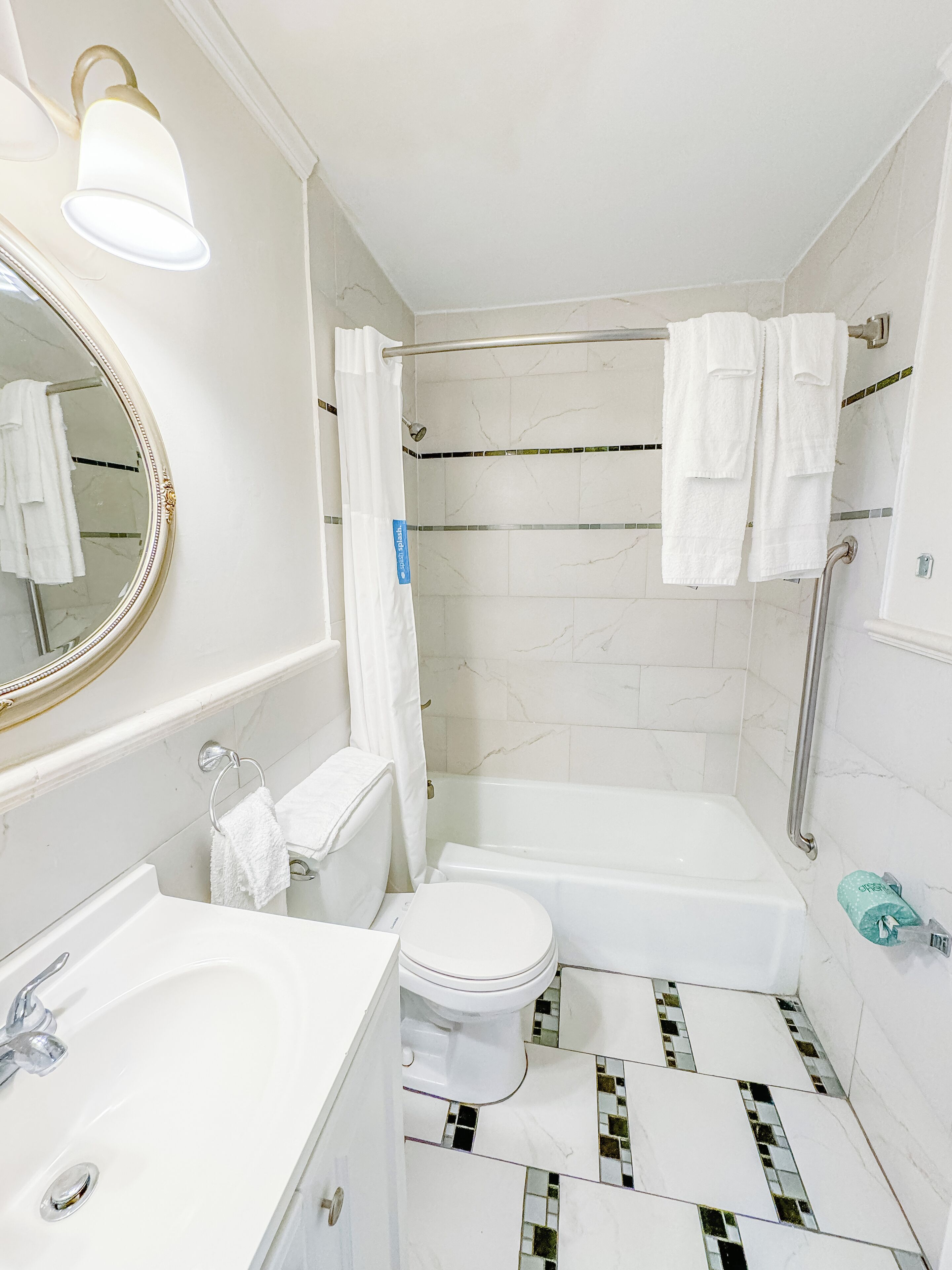 A bathroom with a white sink, toilet, and bathtub. There is a shower curtain, a towel rack, and a mirror with a gold frame.