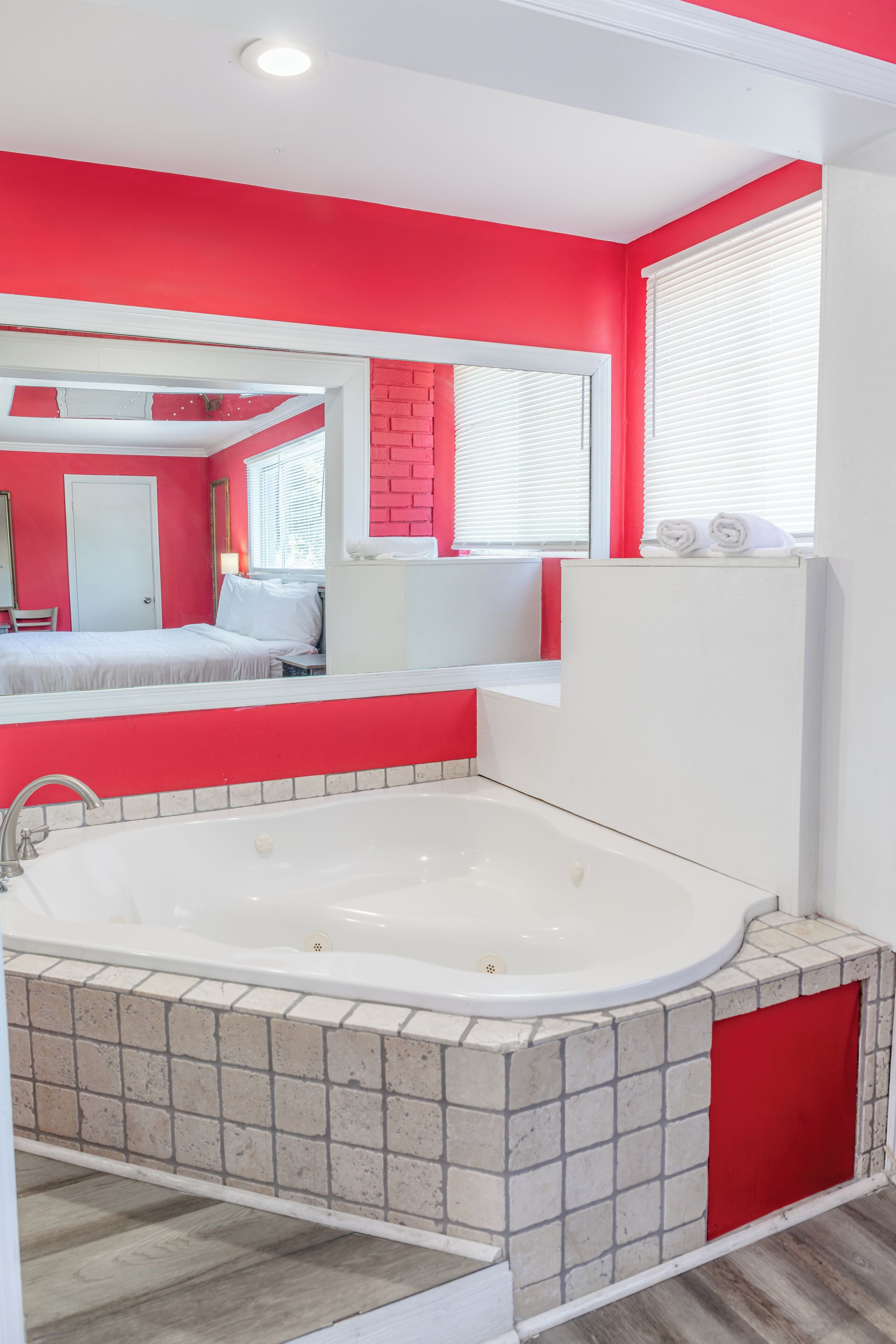 Un baño moderno con una bañera blanca grande, una pared de acento roja y un espejo sobre la bañera.