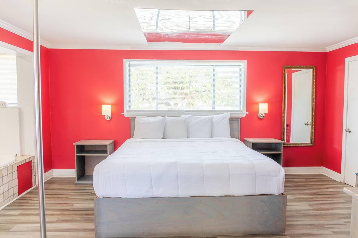 Une chambre à coucher comprenant un lit, deux tables de chevet, une grande fenêtre, un miroir et une lucarne.