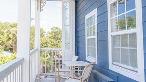 Une véranda abritée avec une table et des chaises, des rampes blanches et une vue sur les arbres et les bâtiments en arrière-plan.