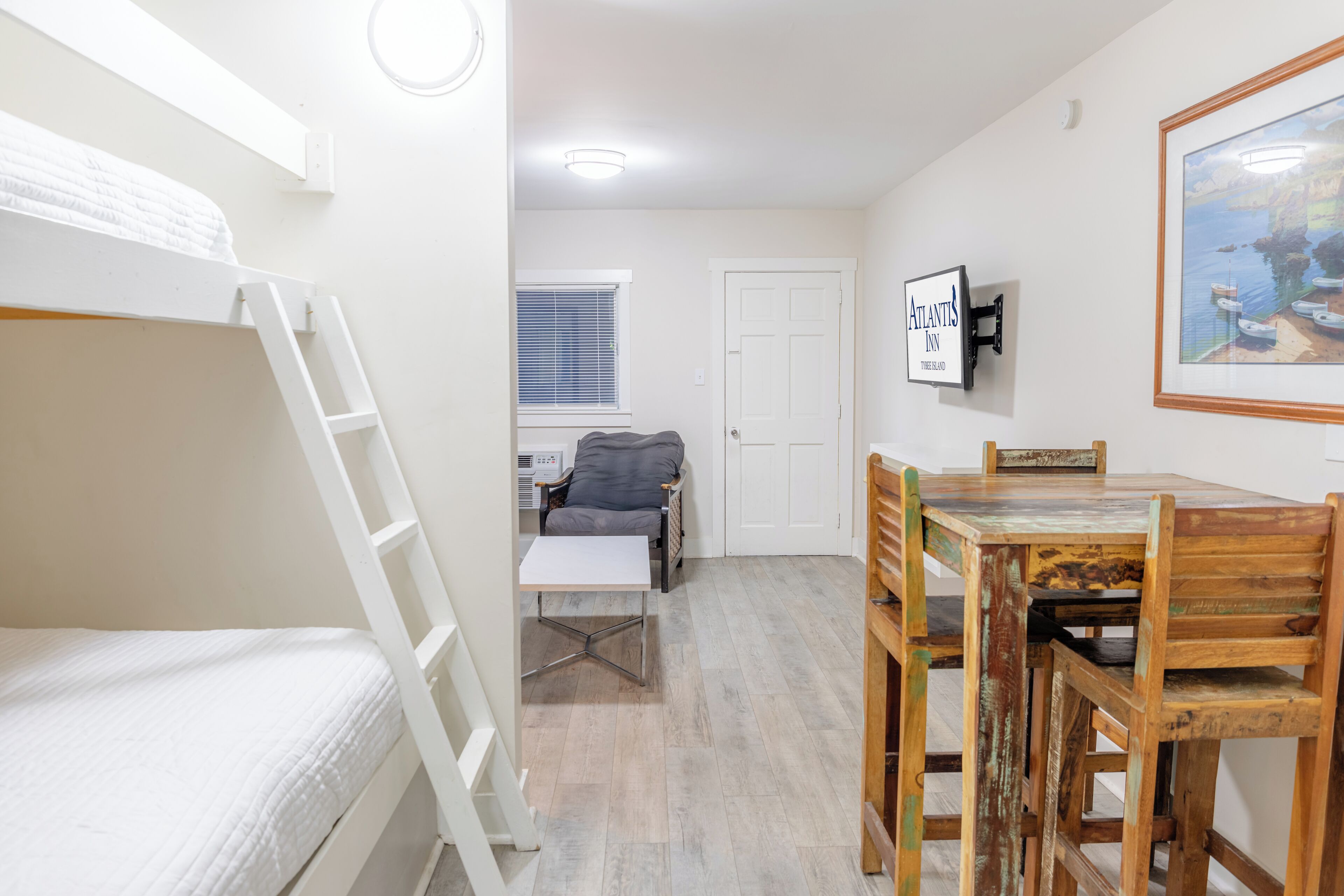 A compact room with bunk beds, a small table, a chair, and a framed picture on the wall.