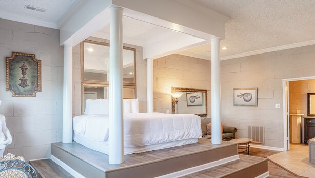 Une chambre dotée d’un lit à baldaquin, d’un coin salon avec une table et une chaise, et offrant une vue sur la salle de bain adjacente.