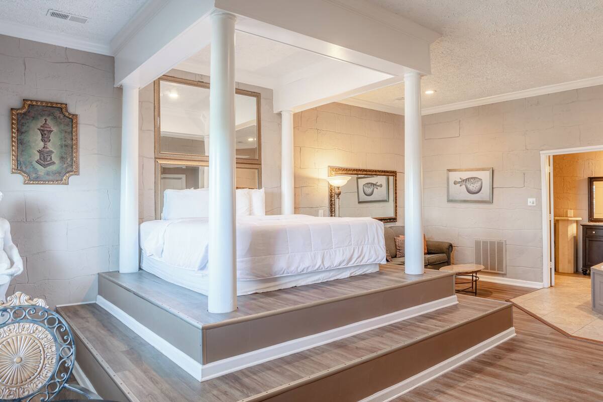 Une chambre dotée d’un lit à baldaquin, d’un coin salon avec une table et une chaise, et offrant une vue sur la salle de bain adjacente.