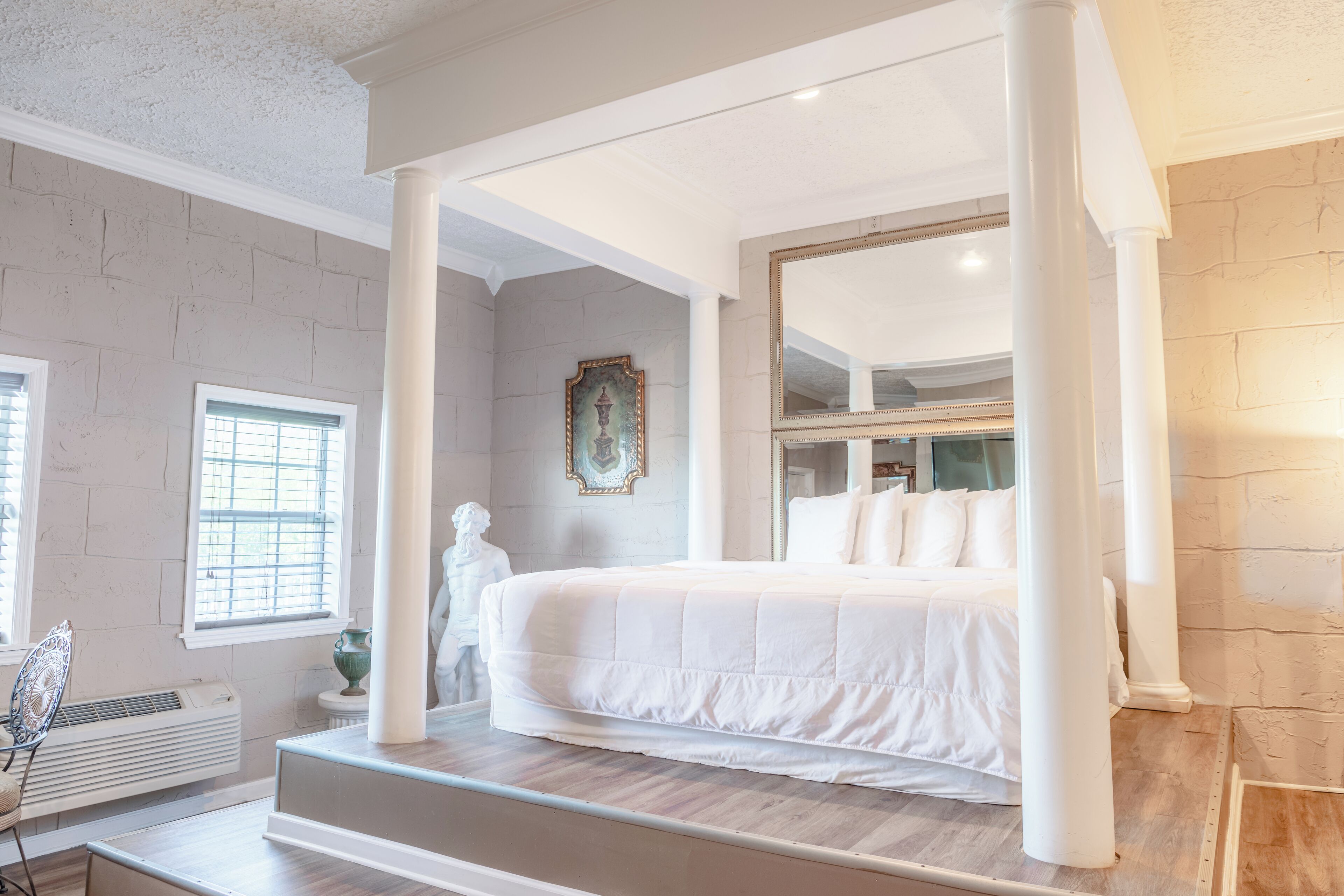 Un dormitorio con cama con dosel, un espejo grande y una estatua.