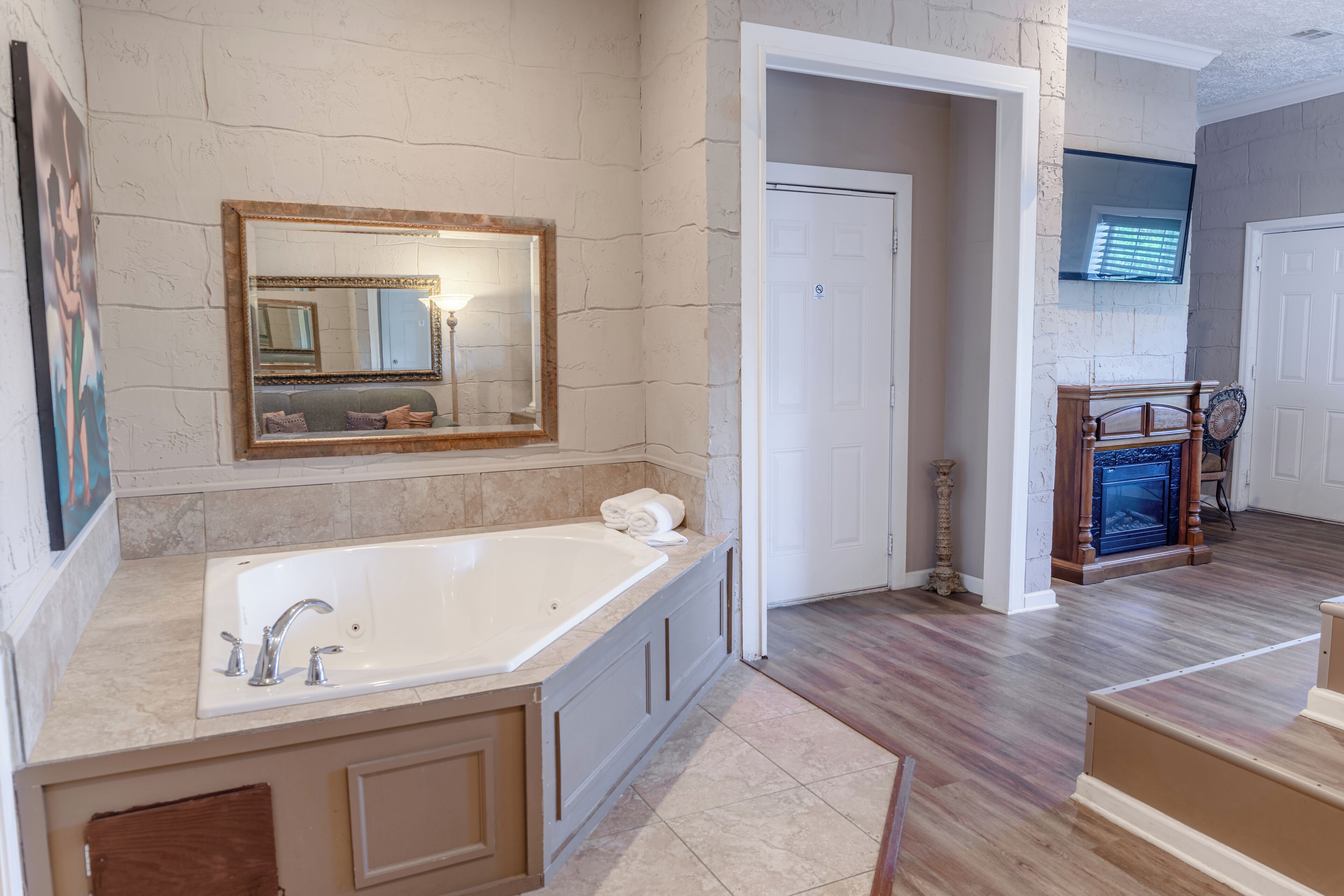 A bathroom with a large bathtub, a mirror, and a door leading to another room.