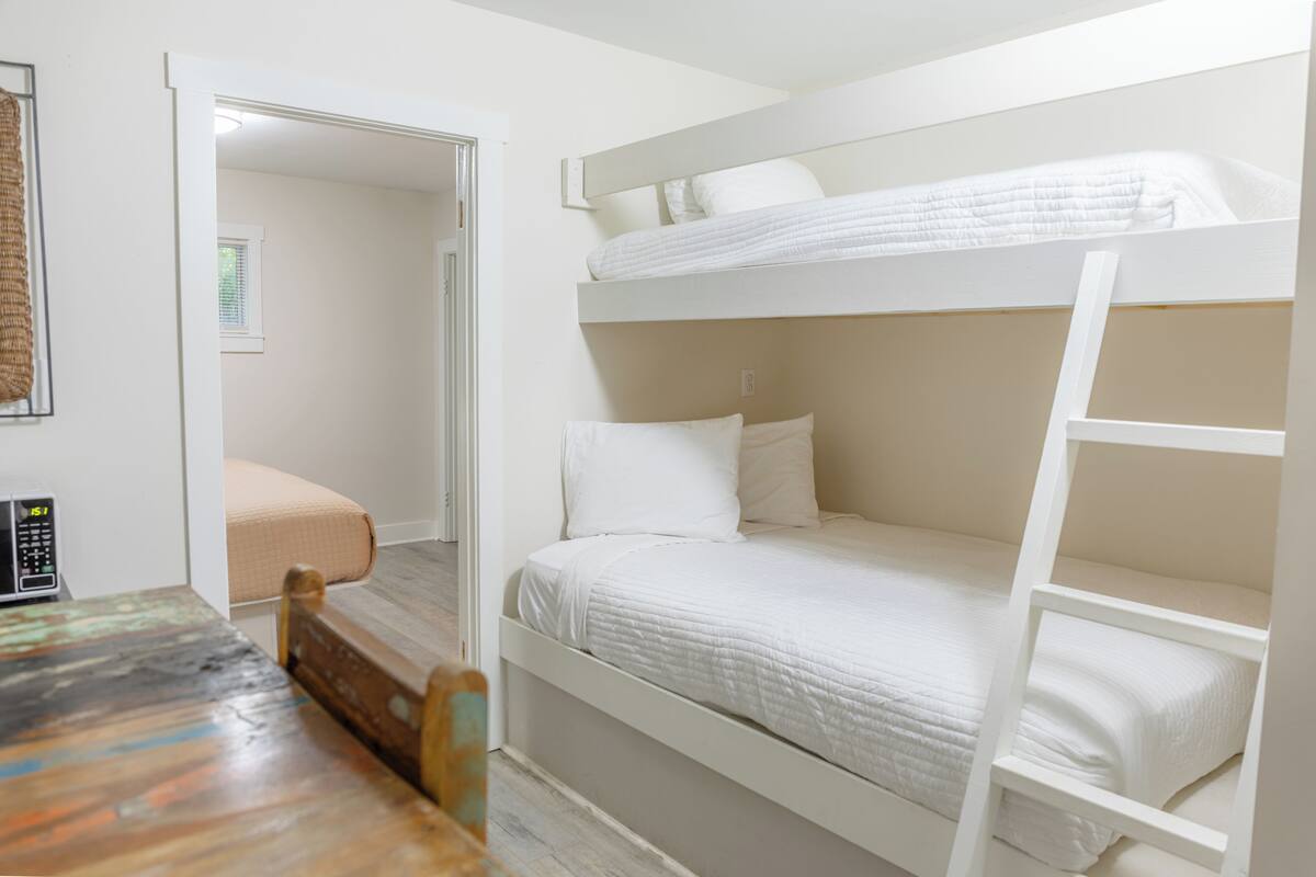 Une chambre avec un lit superposé, une table en bois et une chaise, une petite fenêtre et un micro-ondes posé sur la table.