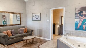 Une salle de bain moderne avec une grande baignoire, un canapé gris agrémenté de coussins à motifs et des œuvres d’art accrochées aux murs.
