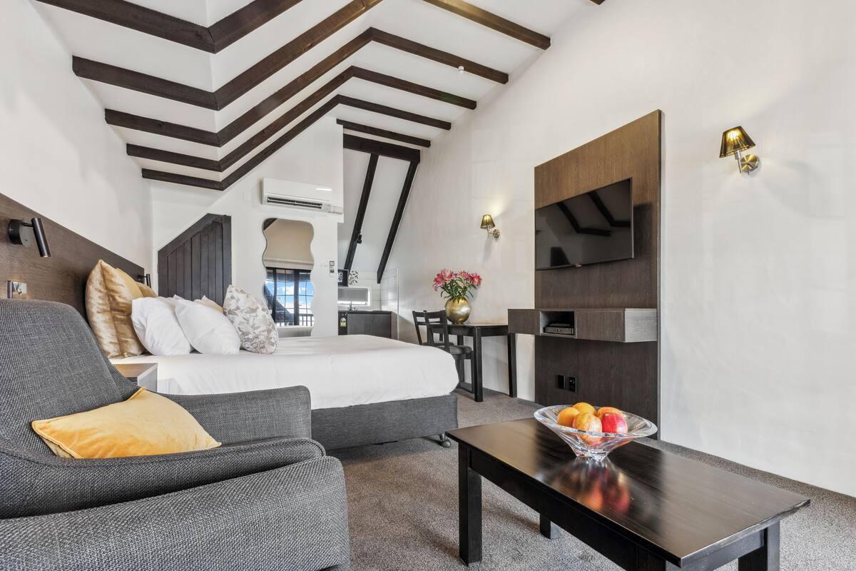Una habitación de hotel moderna con cama, sofá, mesa de comedor y televisor.