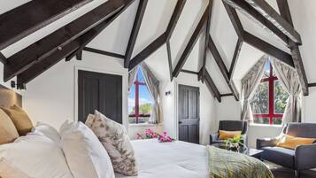 Une chambre à coucher avec un grand lit, deux fauteuils, une petite table et une fenêtre avec des rideaux.