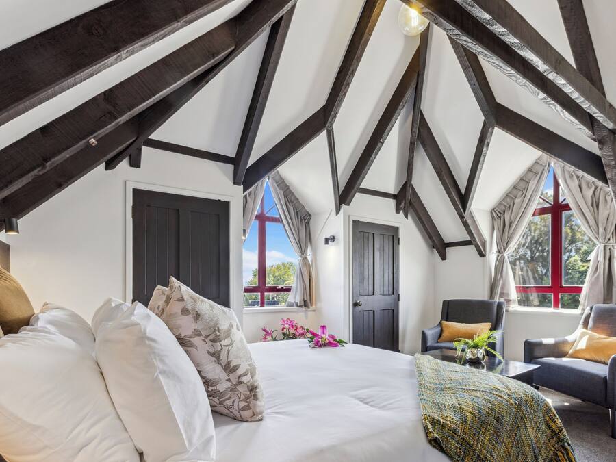 Une chambre à coucher avec un grand lit, deux fauteuils, une petite table et une fenêtre avec des rideaux.