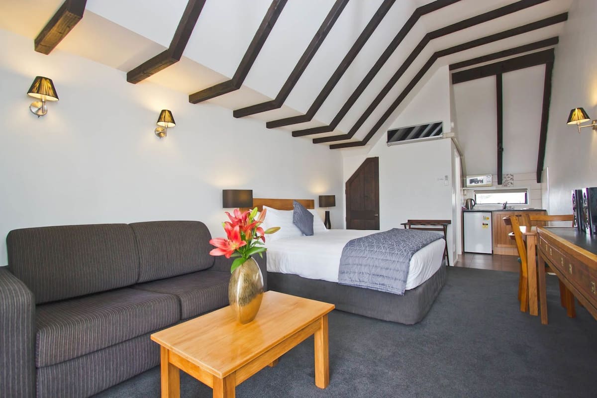 Habitación de hotel moderna con sofá, cama, mesa de madera y kitchenette.