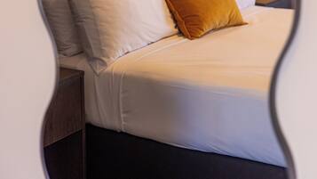 A neatly made bed with white and mustard pillows, a headboard, and a bedside table with a lamp.