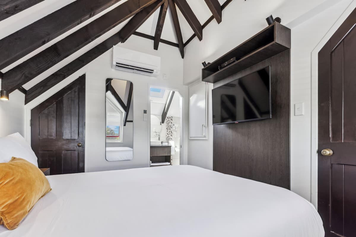 Un dormitorio con una cama grande, vigas de madera oscura, un televisor y una puerta.