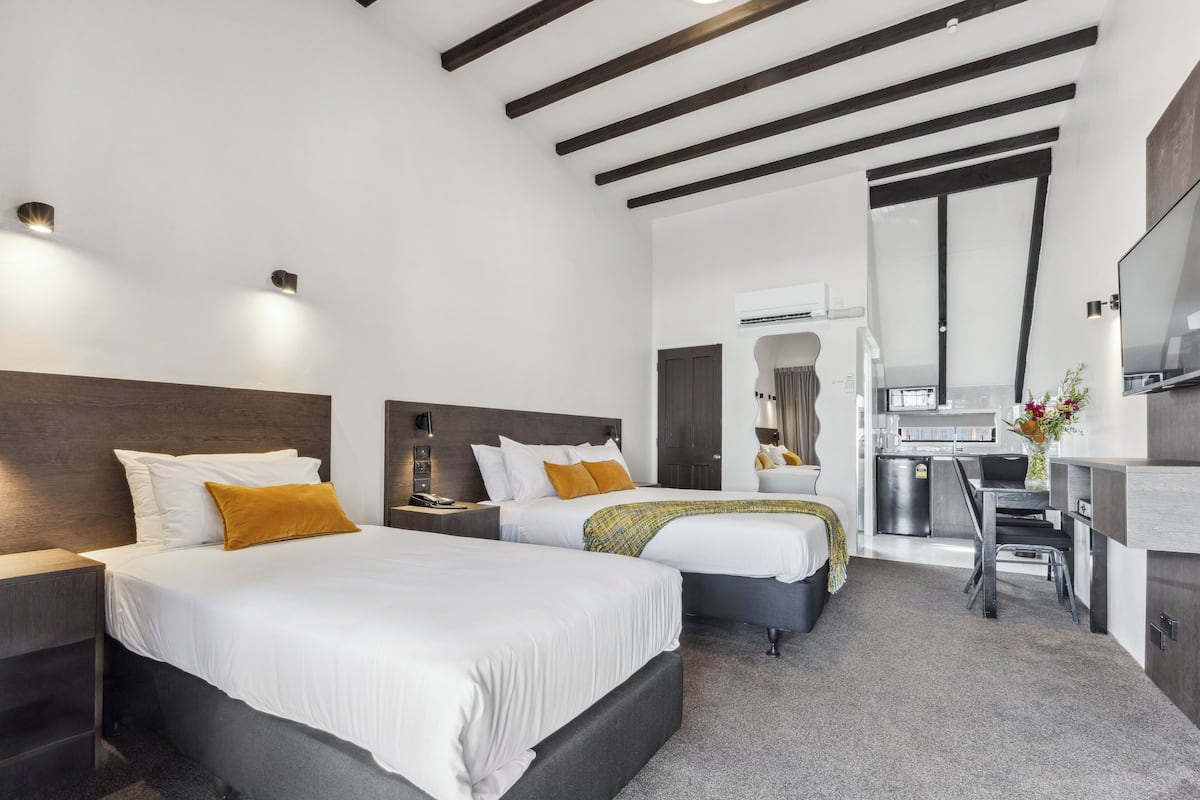 Una habitación de hotel moderna con dos camas, una kitchenette y un televisor.