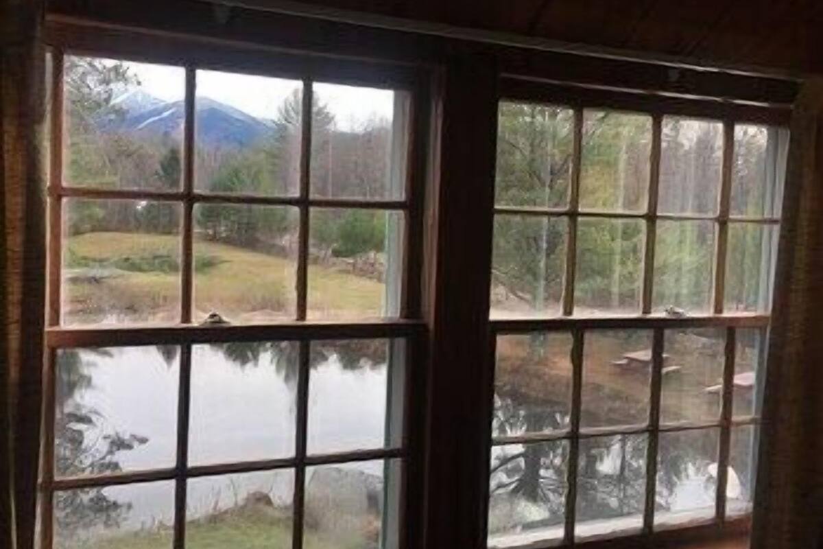 A room with a large window offering a view of a lake and mountains.