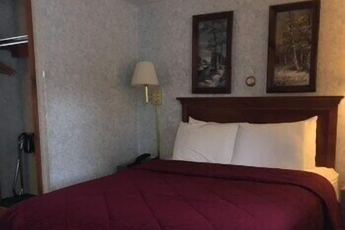 A hotel room with a bed, a nightstand, a lamp, and two framed pictures on the wall.