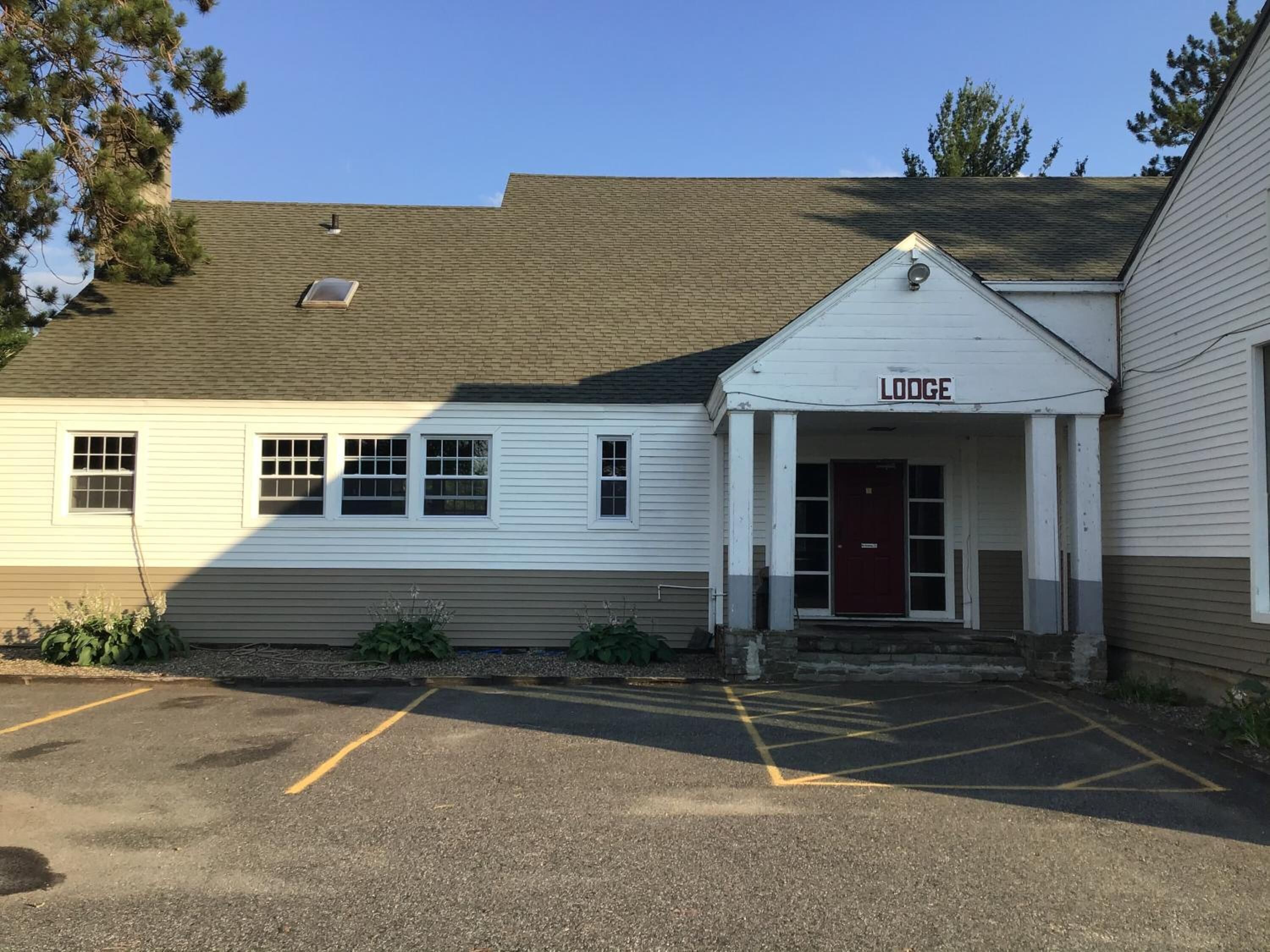A lodge with a white facade, a red door, and a parking lot in front.