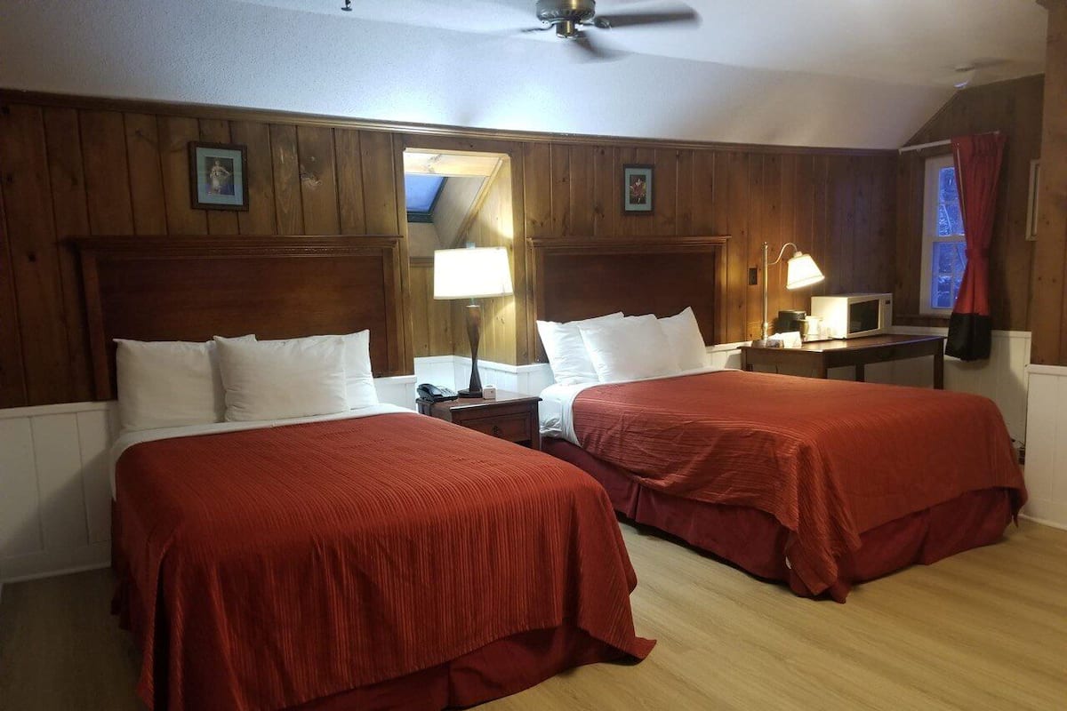 A room with two beds, wooden paneling, a ceiling fan, and a window with curtains.