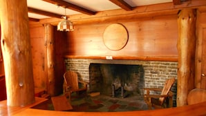 A log cabin interior with a fireplace, wooden furniture, and a hanging light fixture. - Stonybrook Motel & Lodge (Franconia)