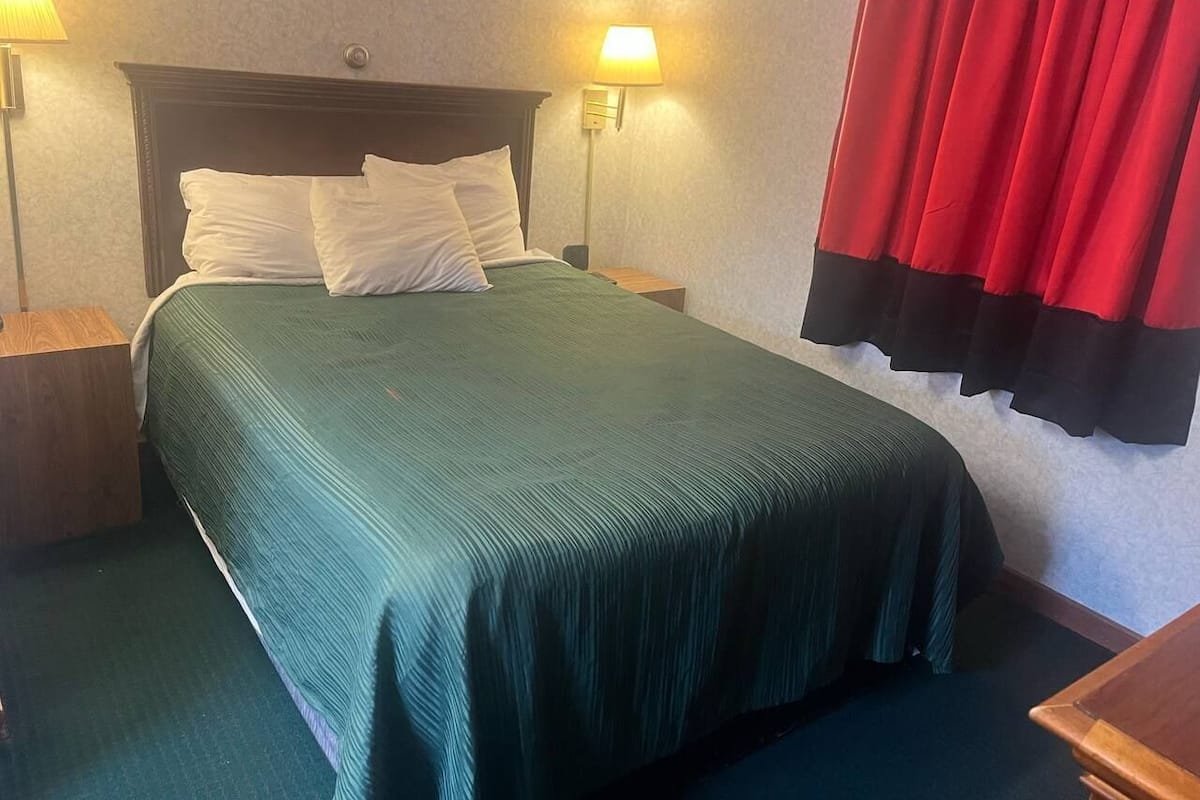 A hotel room with a bed, two bedside lamps, a nightstand, and a red curtain.