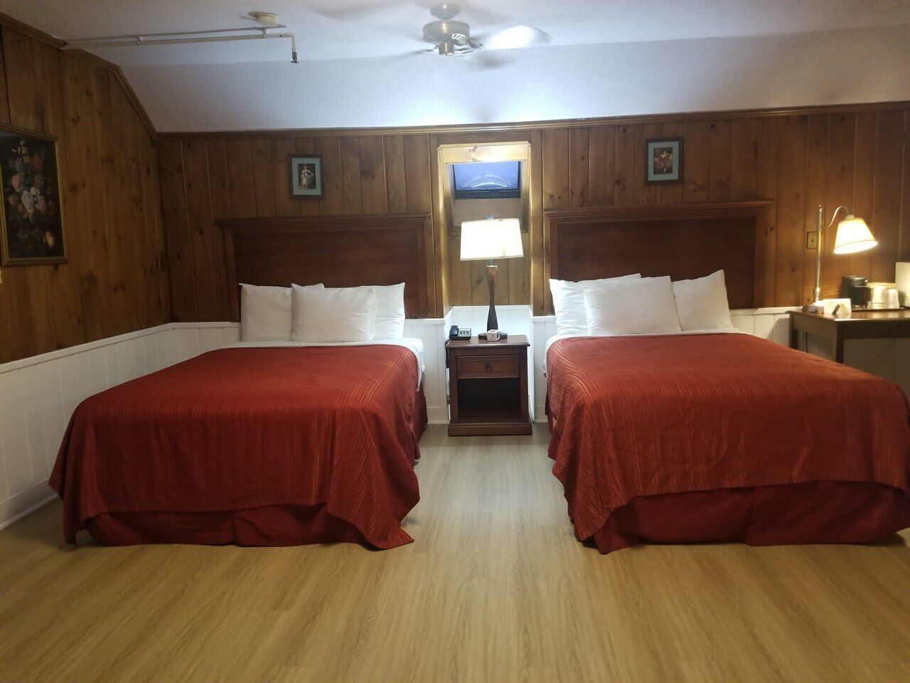 A room with two beds, wooden walls, a ceiling fan, and a television.