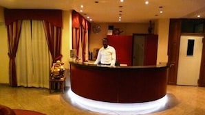 Zona de recepción de un hotel con un mostrador rojo, un hombre de pie detrás y un reloj en la pared.