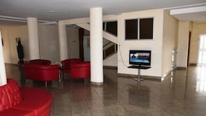 Un vestíbulo amplio con un sofá rojo, un televisor sobre un pedestal y una escalera al fondo.