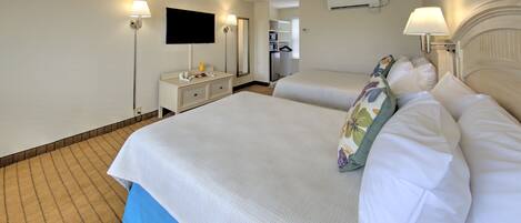A hotel room with two beds, a desk, a TV, and an air conditioning unit.
