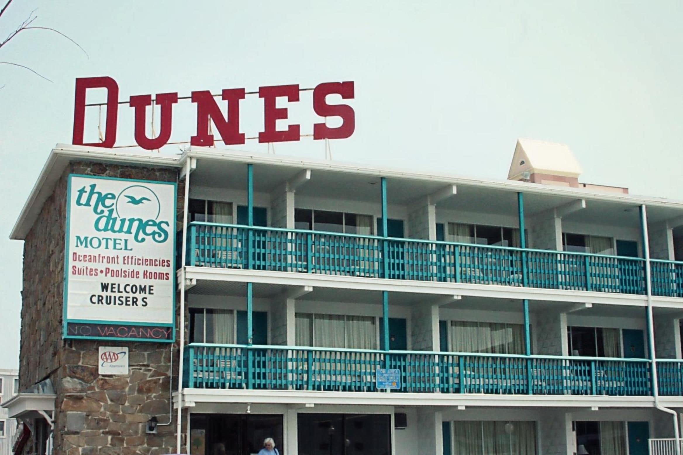 Ein Motel namens 'Dunes' mit einem Schild, das Zimmer mit Meerblick, Suiten und Zimmer am Pool anzeigt.