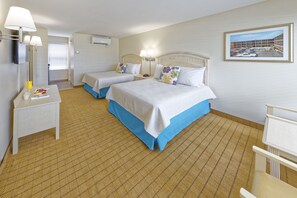 A hotel room with two beds, a small table with a lamp, a bedside table, and a framed picture on the wall.