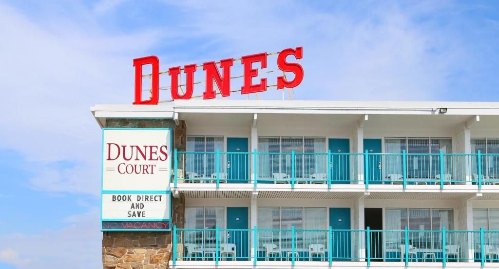 Ett hotell som heter ”DUNES COURT” med en skylt som visar ”BOKA DIREKT OCH SPARA” och ”INGA LEDIGA RUM”.